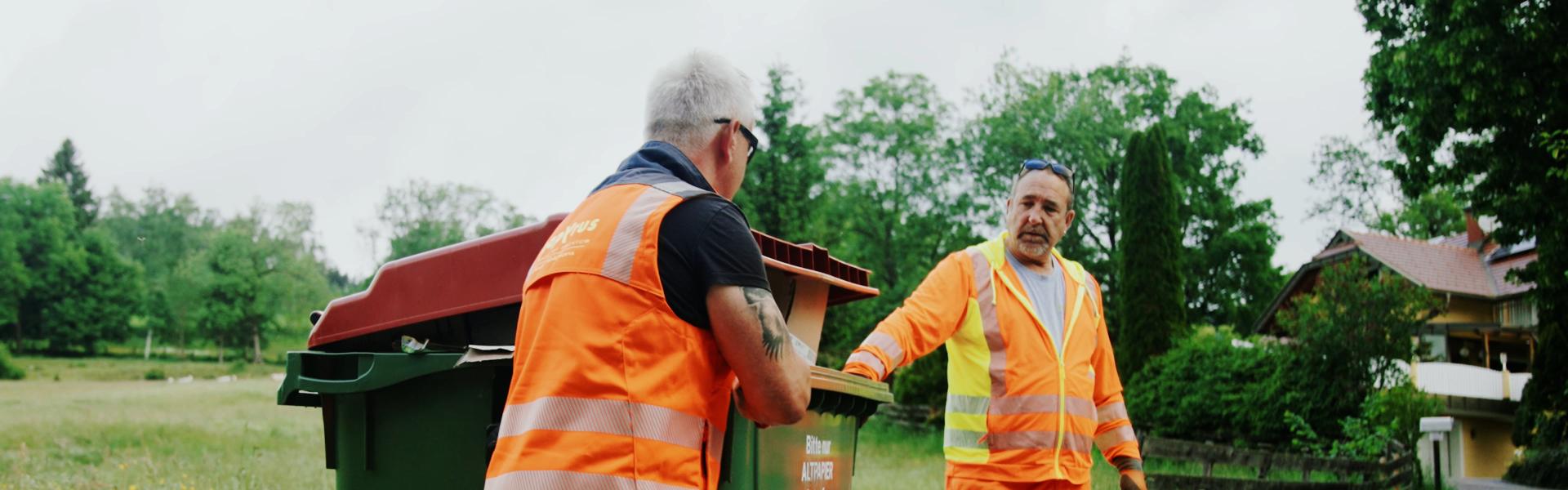 Zwei Männer in Sicherheitsbekleidung entleeren einen 1100 Liter Behälter