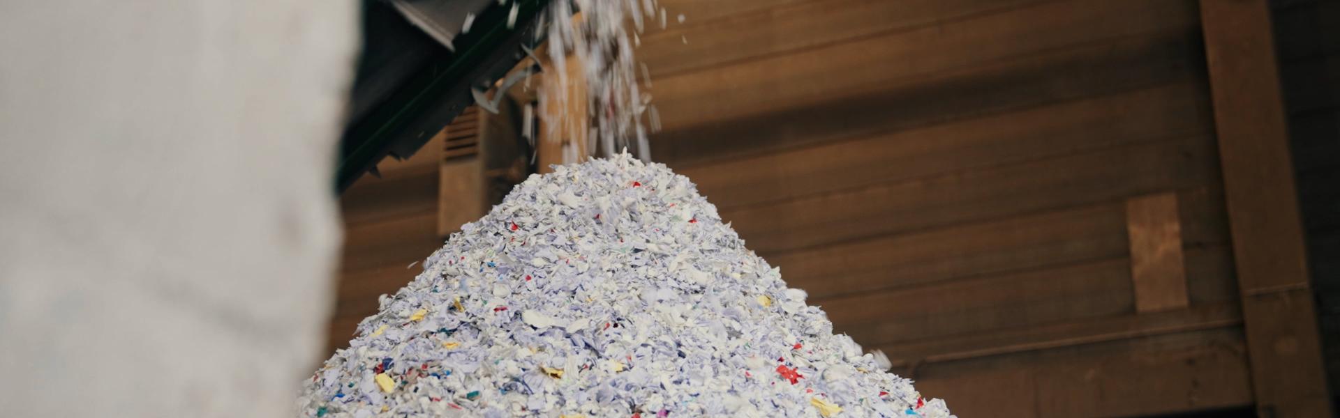 Aktenschnipsel fallen von einem Band auf die bereits geshredderten Akten.